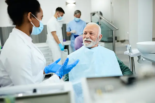 Older patient sitting in dental chair calmly discussing his oral health with his female dentist at Cleary Dental in Haddonfield, NJ